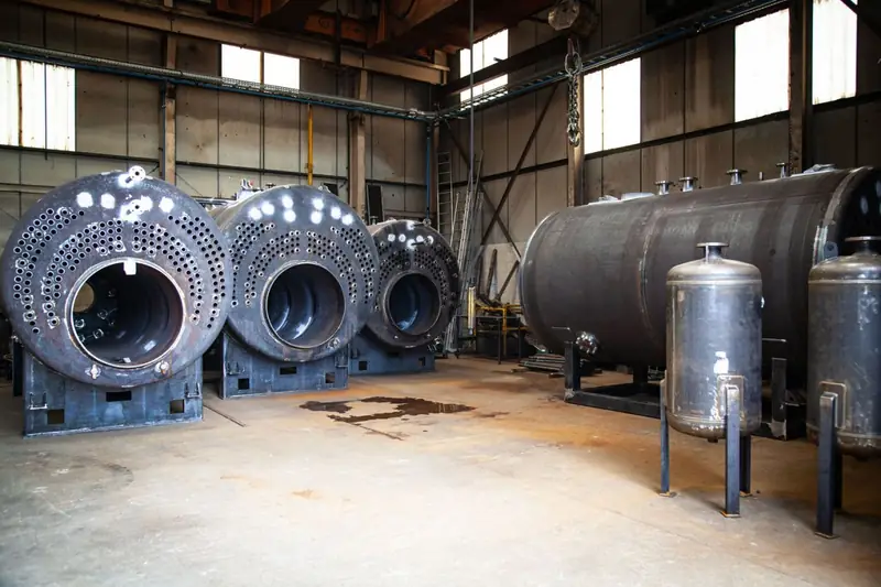 Trois corps de chaudières à plaques tubulaires, un réservoir horizontal et des ballons verticaux dans l'atelier